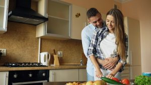 Happy young couple embracing and talking in the kitchen while cooking breakfast at home in the morning